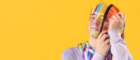 Young man in bandana with drawn stripes on his face and scarf against yellow background, closeup - obrazy, fototapety, plakaty