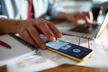 Man checking financial data on smartphone while working on laptop