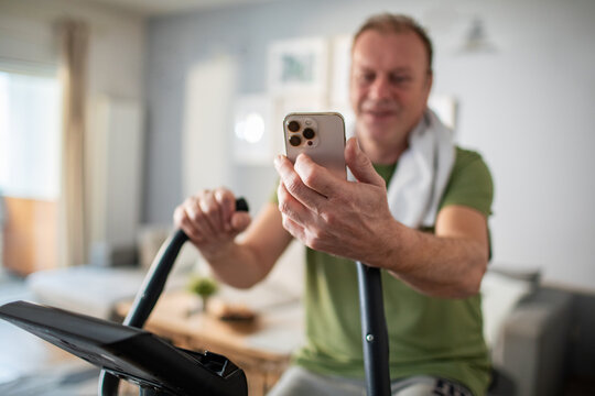 Middle aged man using smartphone on home exercise bike