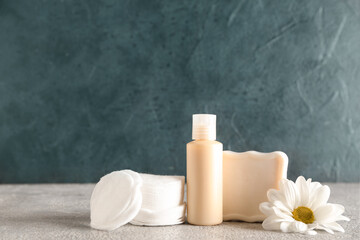 Bottle of cosmetic product, soap, cotton pads and chamomile flower on table