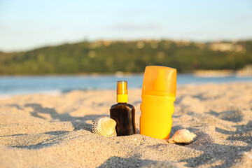 Bottles of sunscreen cream with seashells on sand near ocean at beach