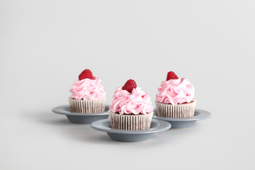 Plates with tasty raspberry cupcakes on grey background
