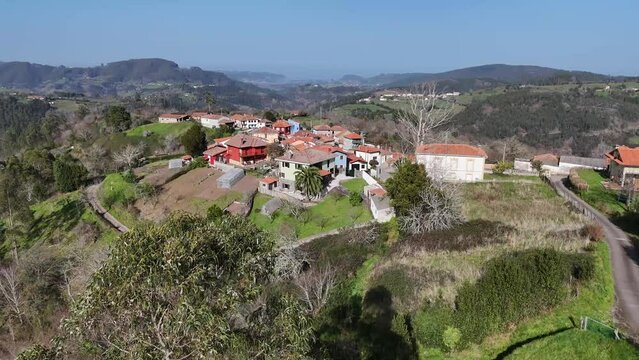 Vista aerea de dron acerc&aacute;ndose en linea recta hacia un pueblo asturiano de casitas viejas vi&eacute;ndose al fondo monta&ntilde;as verdes llenas de arboles y el mar cant&aacute;brico.