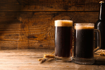 Mugs of dark beer on wooden background