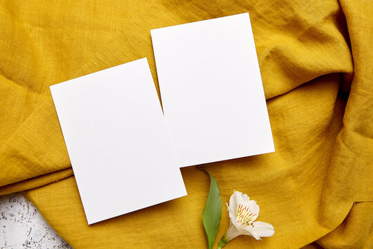 Empty greeting cards and white flower on yellow cloth, top view, flat lay
