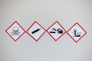 Obraz premium Four hazard warning signs with red diamond borders, depicting toxicity, gas under pressure, corrosion, and environmental hazards, used for safety compliance.
