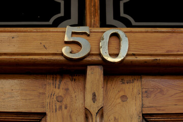 House number 50 with the fifty in bronze on a black wooden front door with panels edged in gold