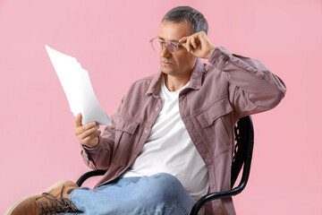 Mature actor reading film script in chair on pink background