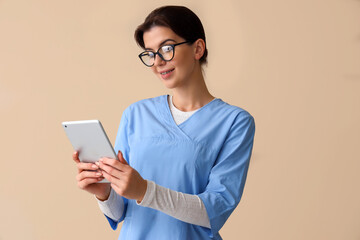 Female medical intern with tablet computer on beige background