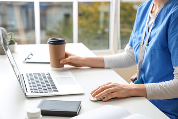 Female doctor with coffee cup working at table in clinic, closeup