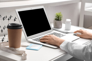 Female doctor working with laptop at table in clinic, closeup