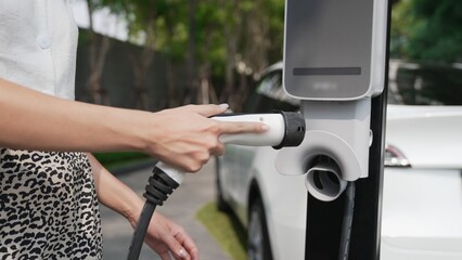 Young woman travel with EV electric car charging in green sustainable city outdoor garden in...