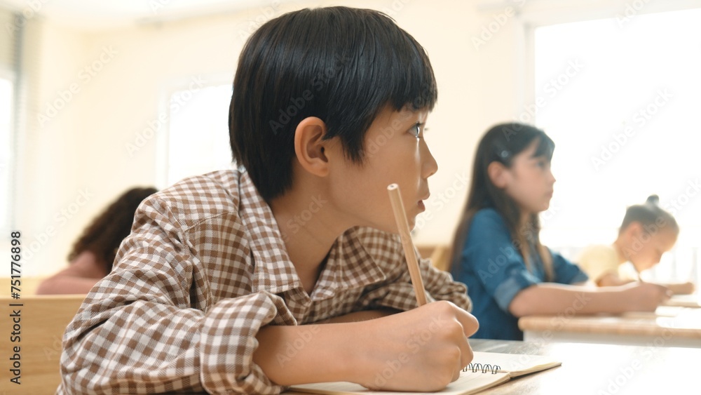Poster close up of skilled asian student writing or taking a note during test. elementary student working o