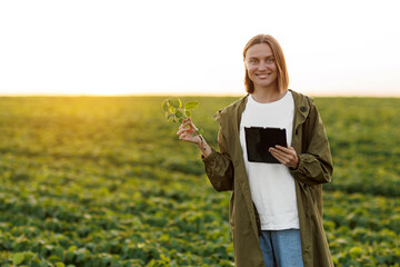 Modern agribusiness. Female farmer holds digital tablet and soya plant in hand in field, examines,...