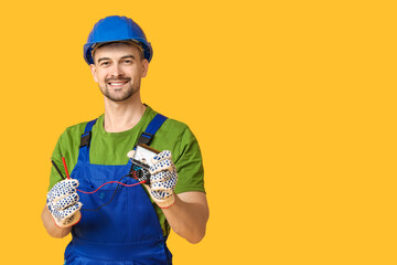 Portrait of male electrician with multimeter on yellow background