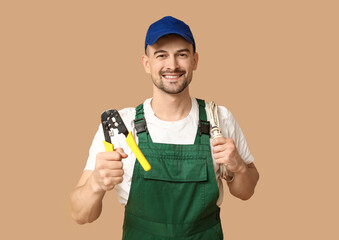 Portrait of male electrician with crimper and wires on beige background