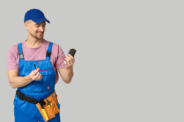 Portrait of male electrician with multimeter on grey background