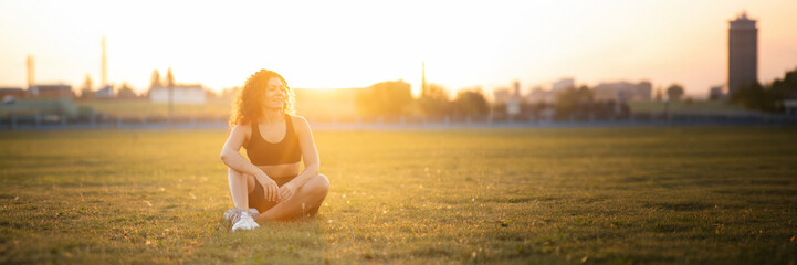athletic positive woman at the stadium at sunset in the summer ready to train.