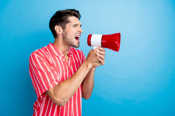 Photo of angry furious guy wear red shirt shouting loud speaker empty space isolated blue color...