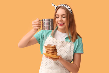 Beautiful young woman adding sugar powder onto tasty pancakes on yellow background