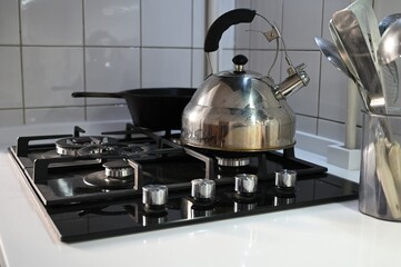 A steel kettle on a gas stove in a kitchen interior decorated with white tiles