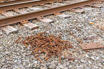 Pile of rusty railroad spikes on crushed stone next to railroad tracks.