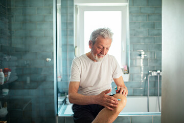 Close up senior man putting ointment on knee in bathroom