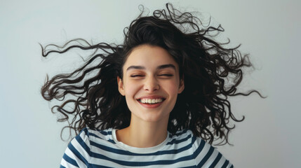 young woman with curly afro hair, wearing a striped shirt, standing with her arms crossed, smiling and looking directly at the camera
