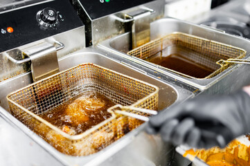 golden-brown fried chicken wings being lifted from a commercial kitchen fryer. The stainless steel...