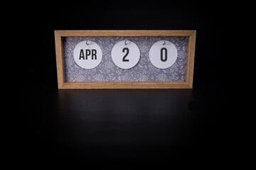 A wooden calendar block showing the date April 20th on a dark black background, save the date or date of an event concept.