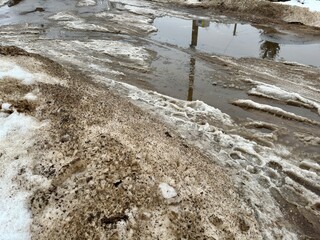 Melting dirty snow on the streets of the city during the daytime in winter. The pedestrian road is snow with sand and mud. Traces of people and pets