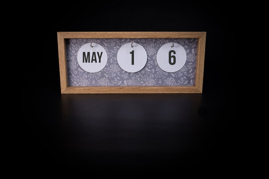 A wooden calendar block showing the date May 16th on a dark black background, save the date or date of an event concept.
