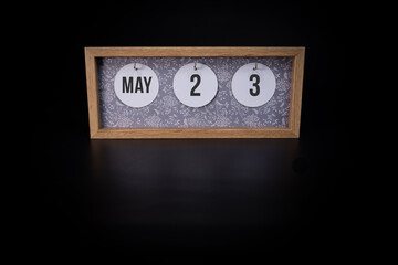 A wooden calendar block showing the date May 23rd on a dark black background, save the date or date of an event concept.