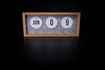 A wooden calendar block showing the date June 9th on a dark black background, save the date or date...