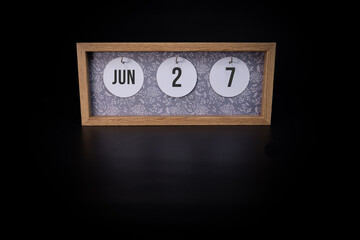 A wooden calendar block showing the date June 27th on a dark black background, save the date or date of event concept