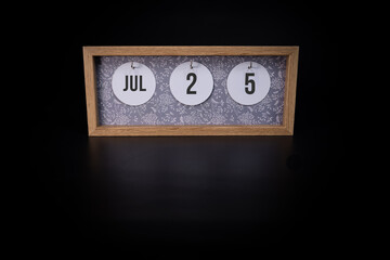 A wooden calendar block showing the date July 25th on a dark black background, save the date or date of event concept