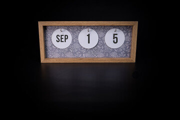 A wooden calendar block showing the date September 15th on a dark black background, save the date or date of event concept