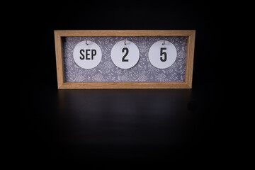 A wooden calendar block showing the date September 25th on a dark black background, save the date or date of event concept