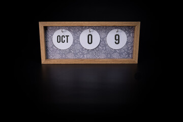A wooden calendar block showing the date October 9th on a dark black background, save the date or date of event concept