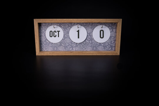 A wooden calendar block showing the date October 10th on a dark black background, save the date or date of event concept
