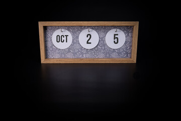 A wooden calendar block showing the date October 25th on a dark black background, save the date or date of event concept