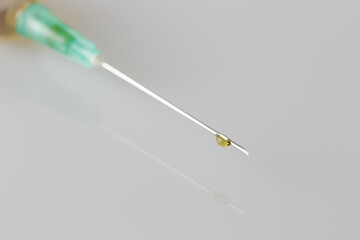 Close-up of the needle of a syringe, with a drop on the needle. Grey background. Horizontal. 