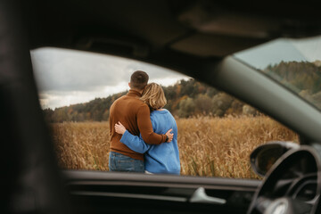 View through the car window, a man and a woman are embracing each other, adult couple enjoying their road trip