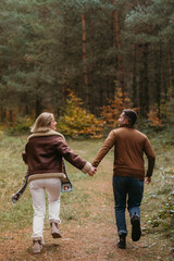 Adult couple having fun together in autumn park, a man and a woman are holding hands while running through the woods