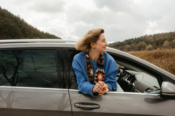 A woman leans out of the car window during road trip in autumn, the wind blows her hair