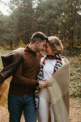 A man and a woman covered in a blanket snuggled up to each other in the middle of the forest, a couple enjoying time together outside the city