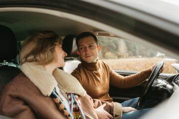 Adult couple on a autumn road trip, man and woman sitting in the car and looking on each other