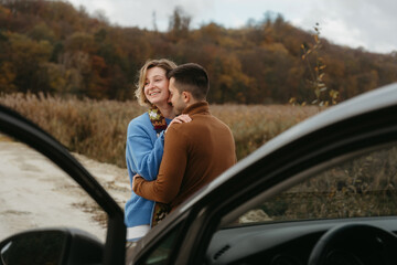 Embracing man and a woman stand next to a car on a dirt road and smiling, couple enjoying roadtrip