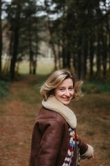 Happy and cheerful adult caucasian woman in a brown jacket is walking through a autumn forest