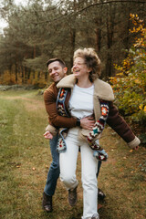 Happy couple is having fun in the middle of the forest, a smiling man hugging his girlfriend in an autumn park.